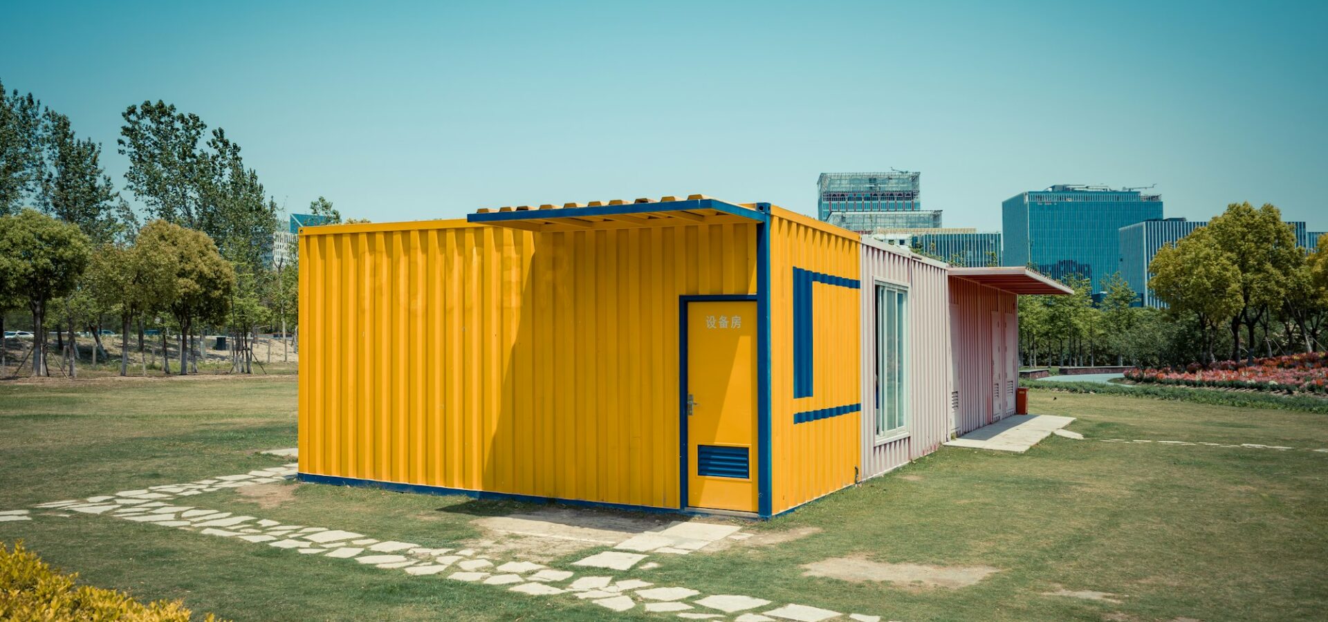 بيت كونتينر للبيع بتصميم عصري ذو واجهة صفراء اللون ومحاط بحديقة خضراء واسعة