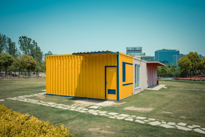 بيت كونتينر للبيع بتصميم عصري ذو واجهة صفراء اللون ومحاط بحديقة خضراء واسعة