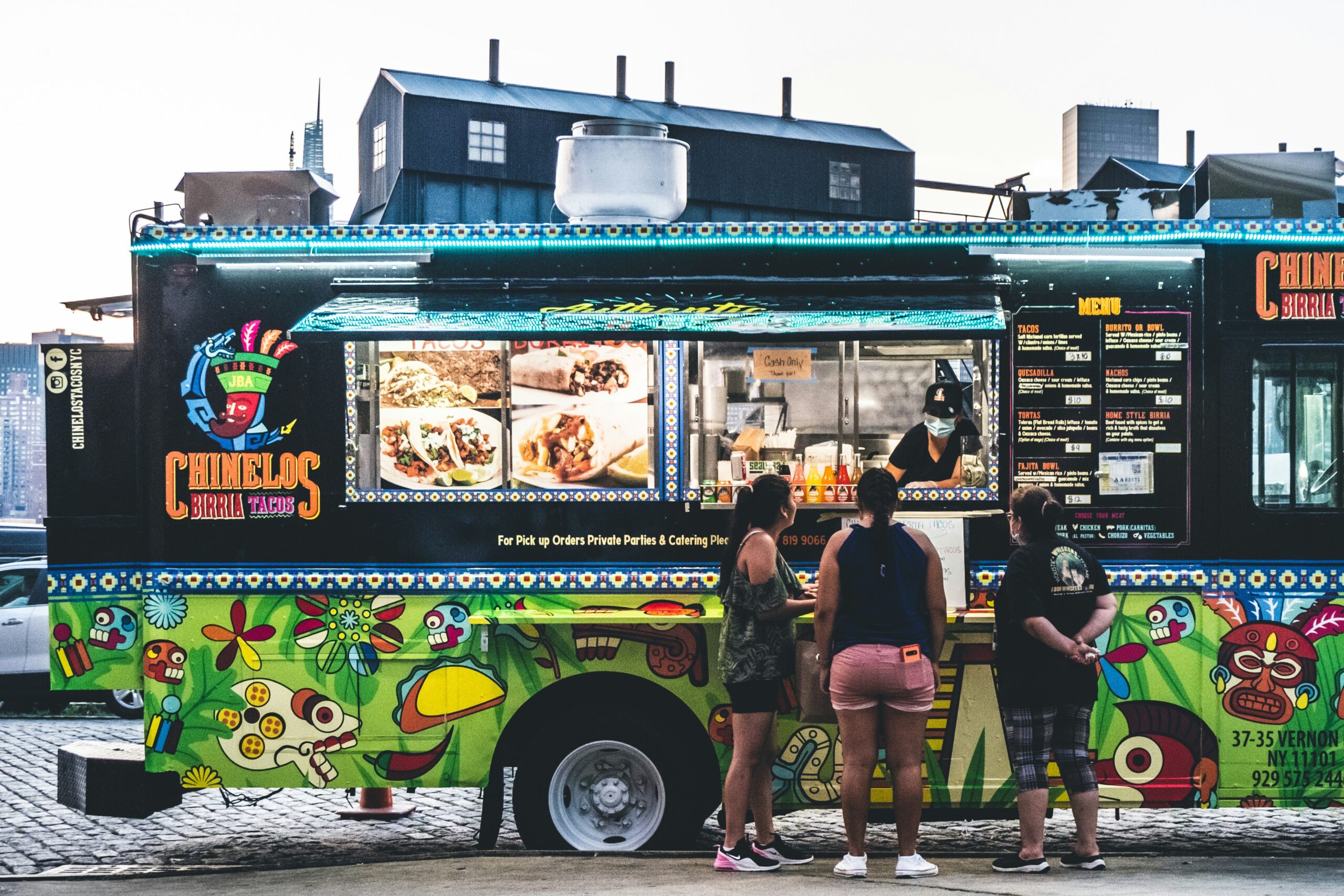 Group of people standing in front of a food truck ordering at the serving window